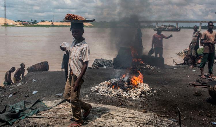 Un niño pasa frene a un punto donde queman basura y materiales de caucho en Yenagoa, Nigeria. Foto: UNICEF/Tanya Bindra